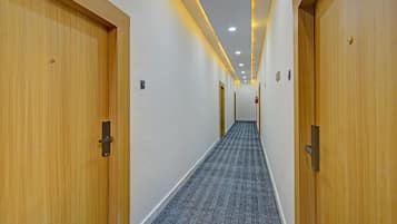 Um corredor de hotel com portas de madeira, piso carpeteado e iluminação embutida no teto.