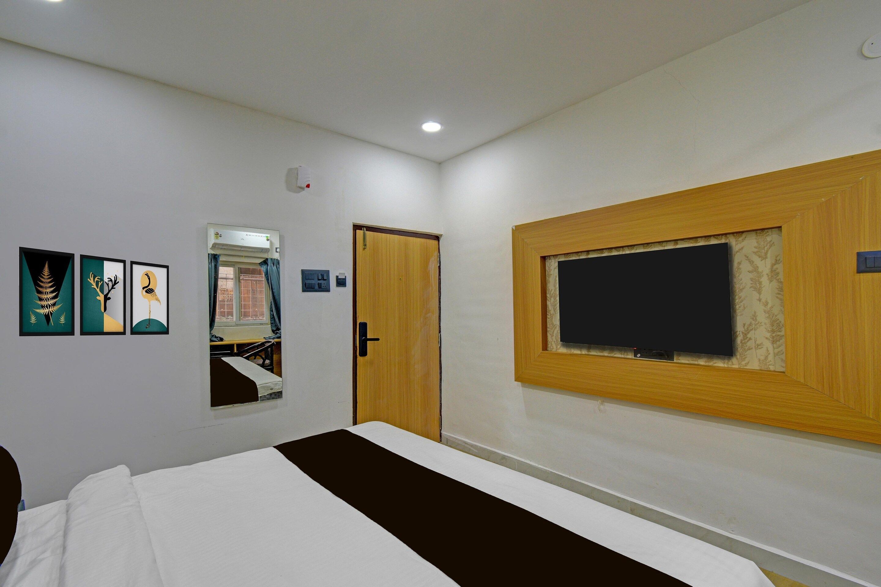 Habitación de hotel con cama, televisor de pared, puerta y ventana con cortinas.