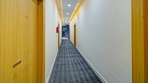 Un couloir d’hôtel avec des portes en bois, un sol recouvert de moquette et un éclairage encastré.