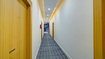Corredor de hotel com portas de madeira, piso coberto de carpete e iluminação embutida.