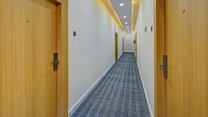 Un couloir d’hôtel avec des portes en bois, un sol recouvert de moquette et des luminaires encastrés au plafond.