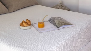 Una cama bien tendida con un cojín, un bol de cruasanes, un vaso de zumo de naranja y un libro en una bandeja.