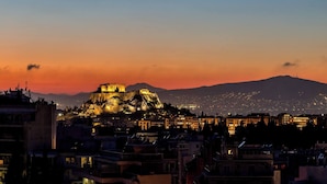 Un paisaje urbano al atardecer con una antigua y destacada ciudadela iluminada sobre una colina, rodeada de edificios modernos.