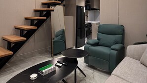 A modern living room with a staircase, a sofa, a coffee table, and a kitchen area. - 101 Tara-jre Al Lweibdeh 2bdr Duplex Apartment (Amman)
