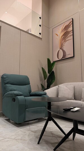 A modern living room with a teal sofa, a grey couch, a glass coffee table, and a large potted plant. - 101 Tara-jre Al Lweibdeh 2bdr Duplex Apartment (Amman)