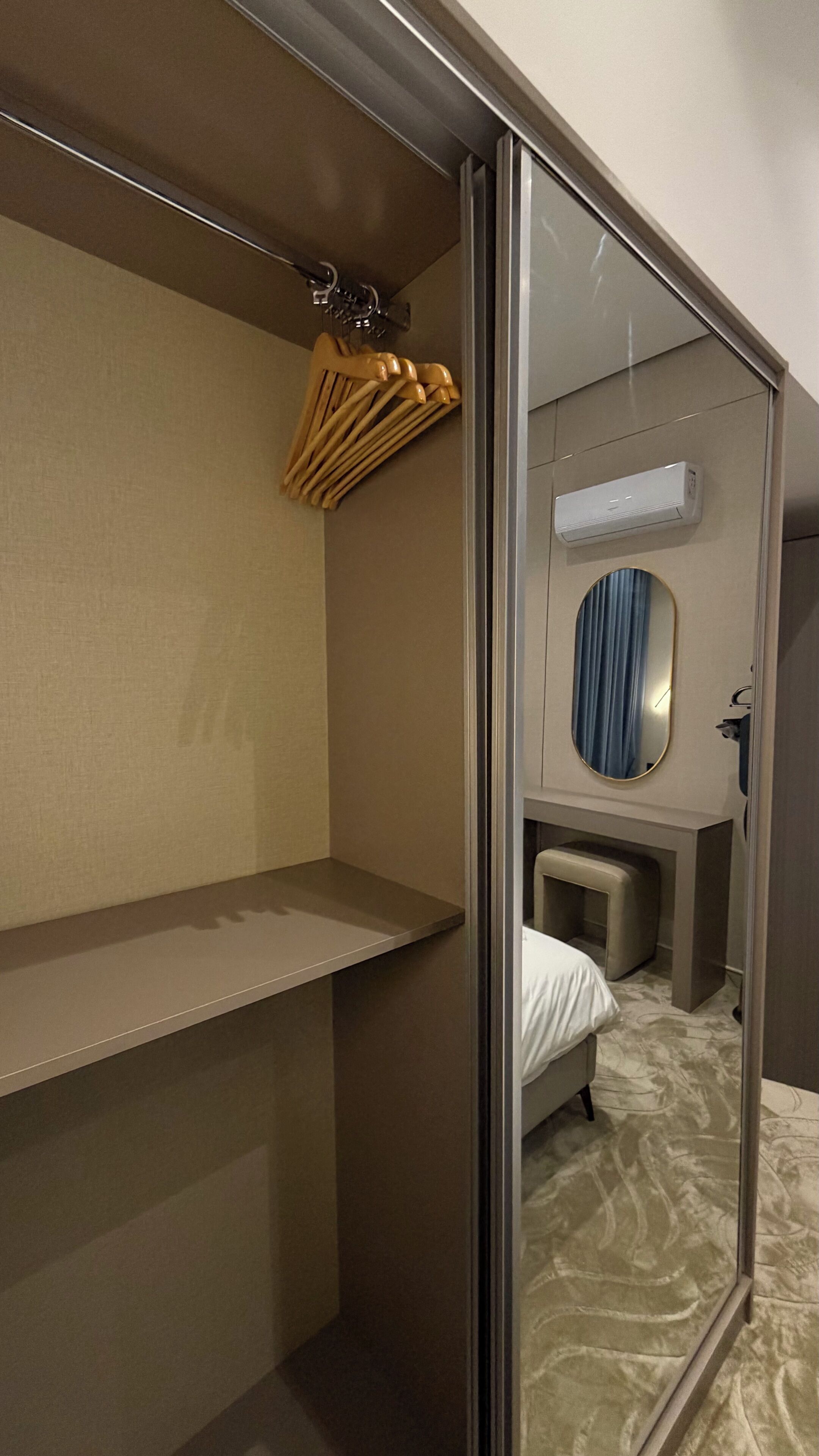 A hotel room with a wardrobe, a mirror, a bed, and a small seating area.