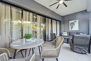 Eine moderne Terrasse im Freien mit einem runden Glastisch, Korbstühlen, einer grauen Couch und einem Deckenventilator.