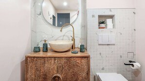 A bathroom with a marble sink, a round mirror, a wooden cabinet, and a small shelf with toiletries. - Cosy & lumineux – 3 pers – Paris centre (Paris)