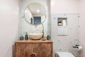A bathroom with a marble sink, a round mirror, a wooden cabinet, and a small shelf with toiletries. - Cosy & lumineux – 3 pers – Paris centre (Paris)