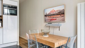 A modern kitchen with a built-in oven, a dining table with clear chairs, and a framed landscape painting on the wall. - Cosy & lumineux – 3 pers – Paris centre (Paris)