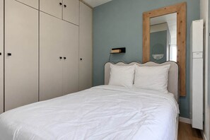 A bedroom with a bed, a wardrobe, a mirror, and a wall-mounted light fixture. - Lumineux cocon pour 3 · Canal Saint-Martin (Paris)