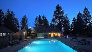 A swimming pool with a clear blue water surface, surrounded by trees and a building with illuminated windows. - Cozy Resort Hideaway (Bend)