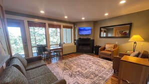A living room with a sofa, a coffee table, a fireplace, a television, and a large window. - Cozy Resort Hideaway (Bend)