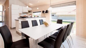 A modern kitchen with white cabinets, a microwave, and a dining area with a white table and black chairs. - 4 Star Holiday Home in Grossenbrode (Grossenbrode)