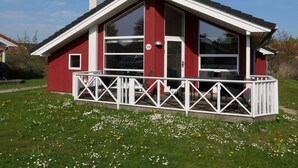 A red building with a white roof, a chimney, and a fenced porch with chairs. - 4 Star Holiday Home in Grossenbrode (Grossenbrode)