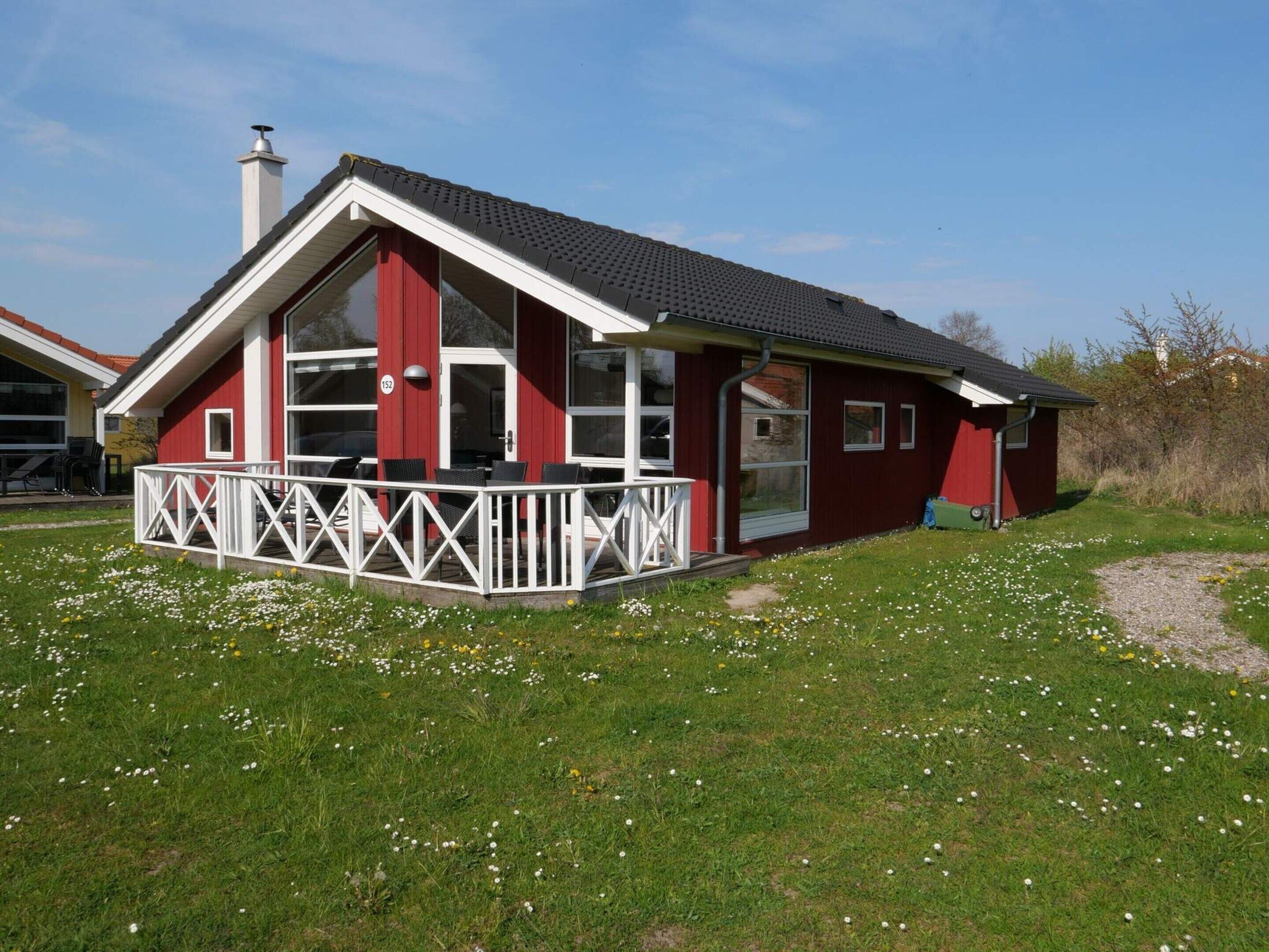 A red building with a white balcony, a chimney, and a grassy area with flowers.