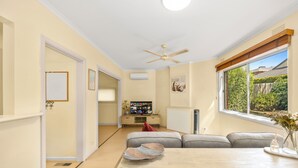 Un salon moderne avec un canapé, une table à manger, un ventilateur de plafond et une fenêtre donnant sur l’extérieur.