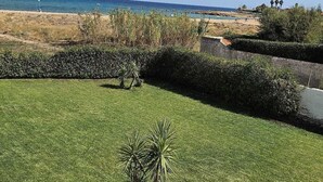 A well-maintained grassy area with a palm tree, a clear blue sky, and a distant view of the ocean. - B&B Mariella Fronte mare (Avola)