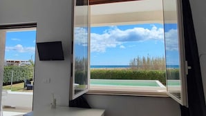 A room with a desk, chair, and a large window with a view of the beach and ocean. - B&B Mariella Fronte mare (Avola)