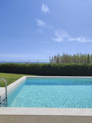 A swimming pool with a clear blue sky, a hedge, and a fence in the background. - B&B Mariella Fronte mare (Avola)