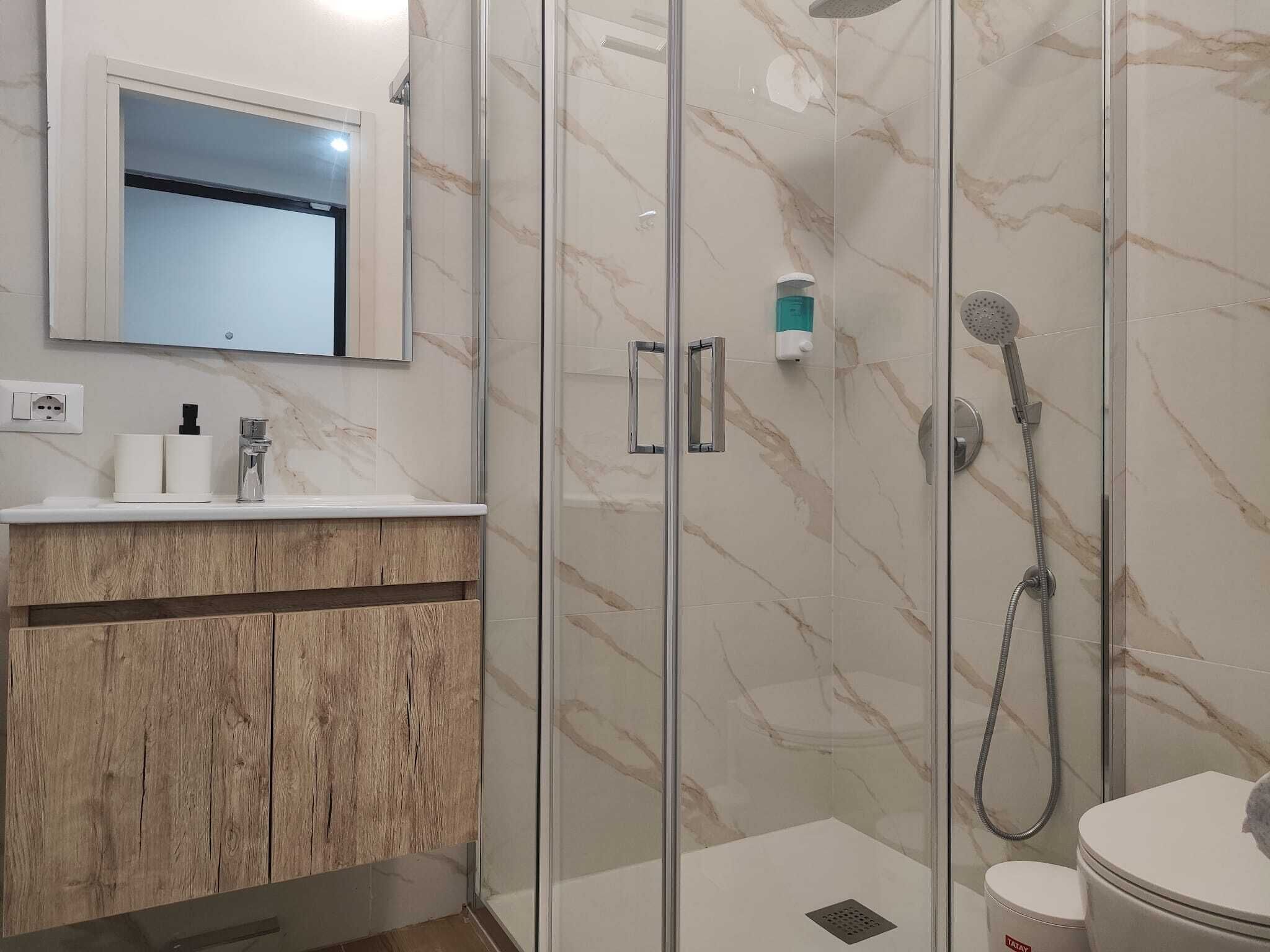 A modern bathroom with a glass shower enclosure, a toilet, and a vanity with a mirror.