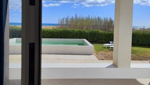 A view through a window of a pool area with a clear sky, a grassy lawn, and a hedge. - B&B Mariella Fronte mare (Avola)
