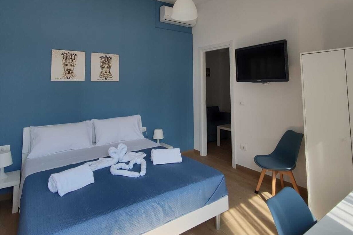 Ein Hotelzimmer mit Bett, Schreibtisch, Stuhl, Fernseher und Bildern an der Wand.