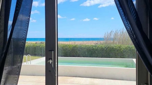 A window with curtains, a view of a beach, and a clear sky. - B&B Mariella Fronte mare (Avola)
