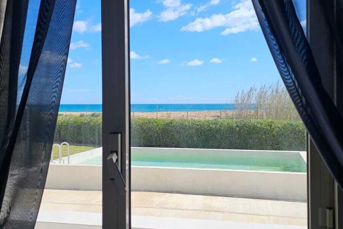 Ein Fenster mit Vorhängen, Blick auf einen Strand und einen klaren Himmel.