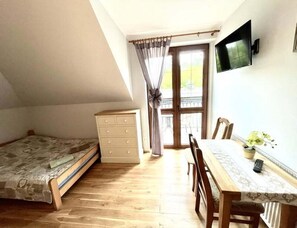 A bedroom with a bed, a dresser, a table with chairs, a TV, and a window with curtains. - Triple Room, Sauna, Masuria (Ruciane-Nida)