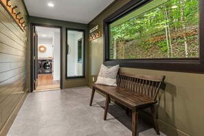 A hallway with a bench, a window with a forest view, and a door leading to a laundry area. - 3-bedroom house in lovely Pittsfield close to wedding venues, trails and skiing! (Pittsfield)