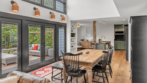 Eine moderne Küche mit einer großen Kochinsel, einem Essbereich mit einem Holztisch und Stühlen sowie Blick durch große Glastüren auf eine Außenpatio.