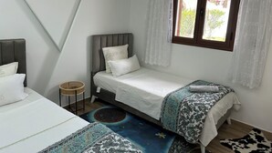 Ein Schlafzimmer mit einem Einzelbett, einem Fenster mit Vorhängen, einem kleinen runden Tisch und einem gemusterten Teppich.