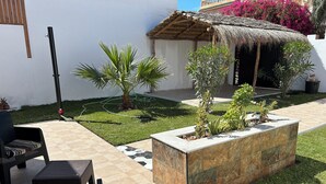 Eine Terrasse mit Gartenmöbeln, ein Garten mit verschiedenen Pflanzen und ein Gebäude mit einem Reetdach.
