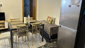 Ein gemütlicher Raum mit Esstisch, Stühlen, einem Kühlschrank, einem Bett und einem Fernseher.