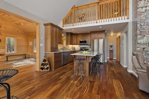 A spacious kitchen with wooden cabinetry, a central island with stools, and a stone accent wall. - Beautiful Comfortable Modern Home on a Quiet Lake surrounded by wilderness. (Baysville)