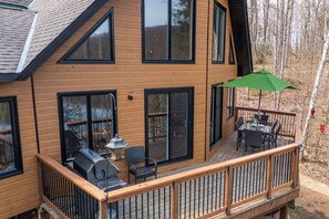 A wooden deck with a grill, outdoor seating, and a green umbrella. - Beautiful Comfortable Modern Home on a Quiet Lake surrounded by wilderness. (Baysville)