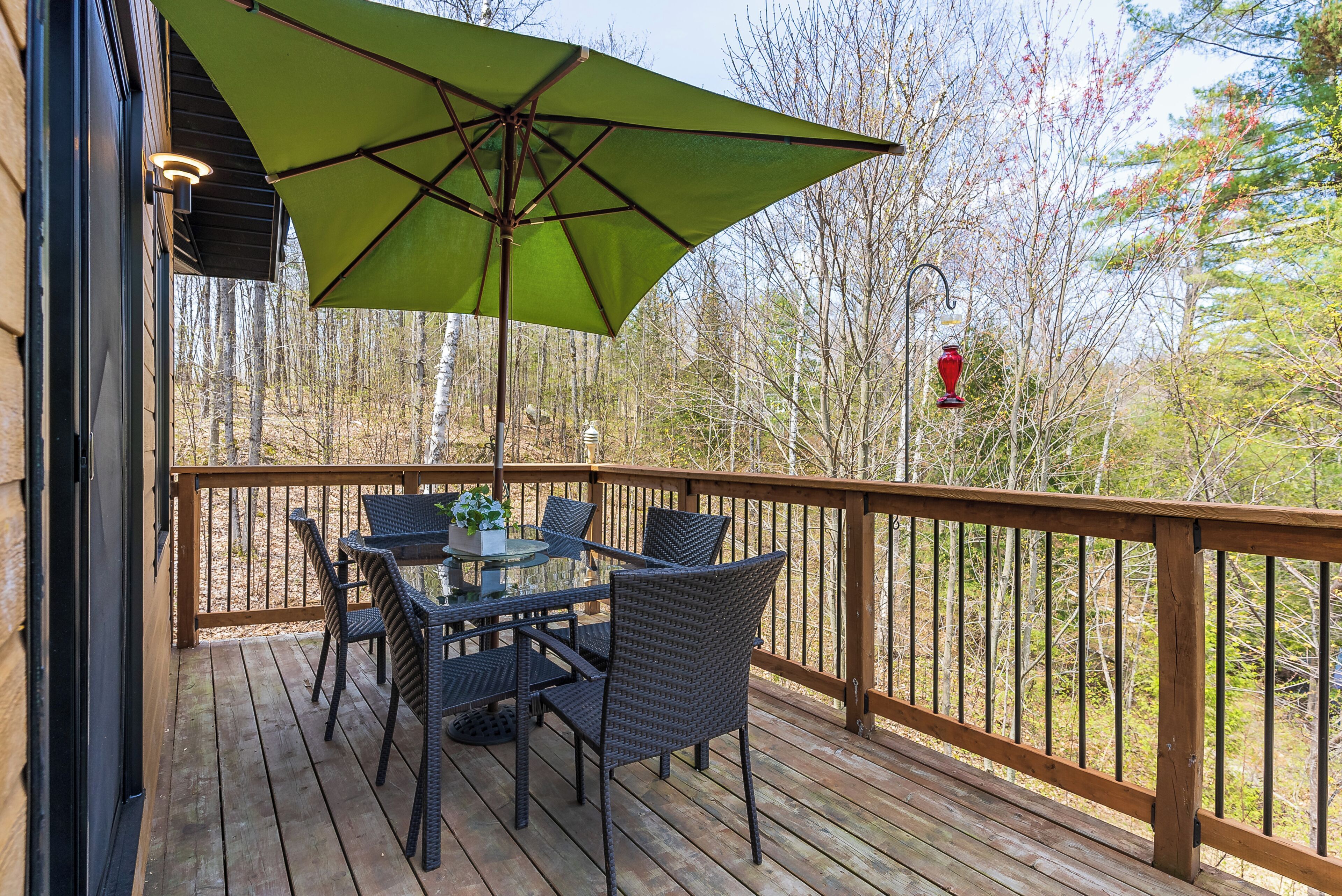 A wooden deck with a table and chairs, a green umbrella, and a railing.