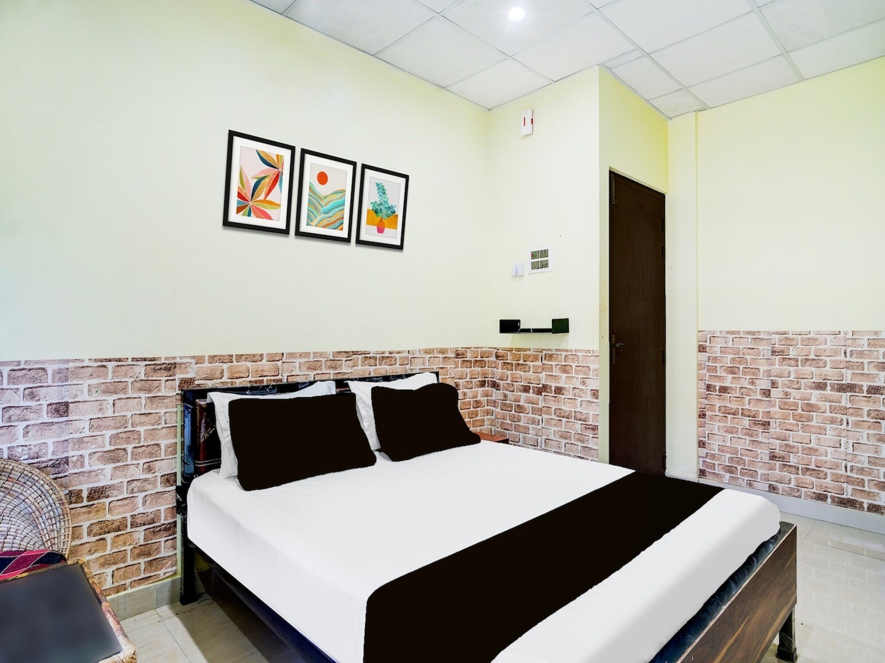 A bed with a white and black bedspread, a brick accent wall, and three framed artworks on the wall.