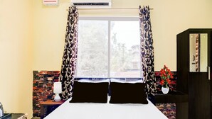 A hotel room with a bed, air conditioning unit, window with curtains, brick wall, and a small table with a vase of flowers. - Classic With Balcony Ganeshguri Nayanpur (Guwahati)