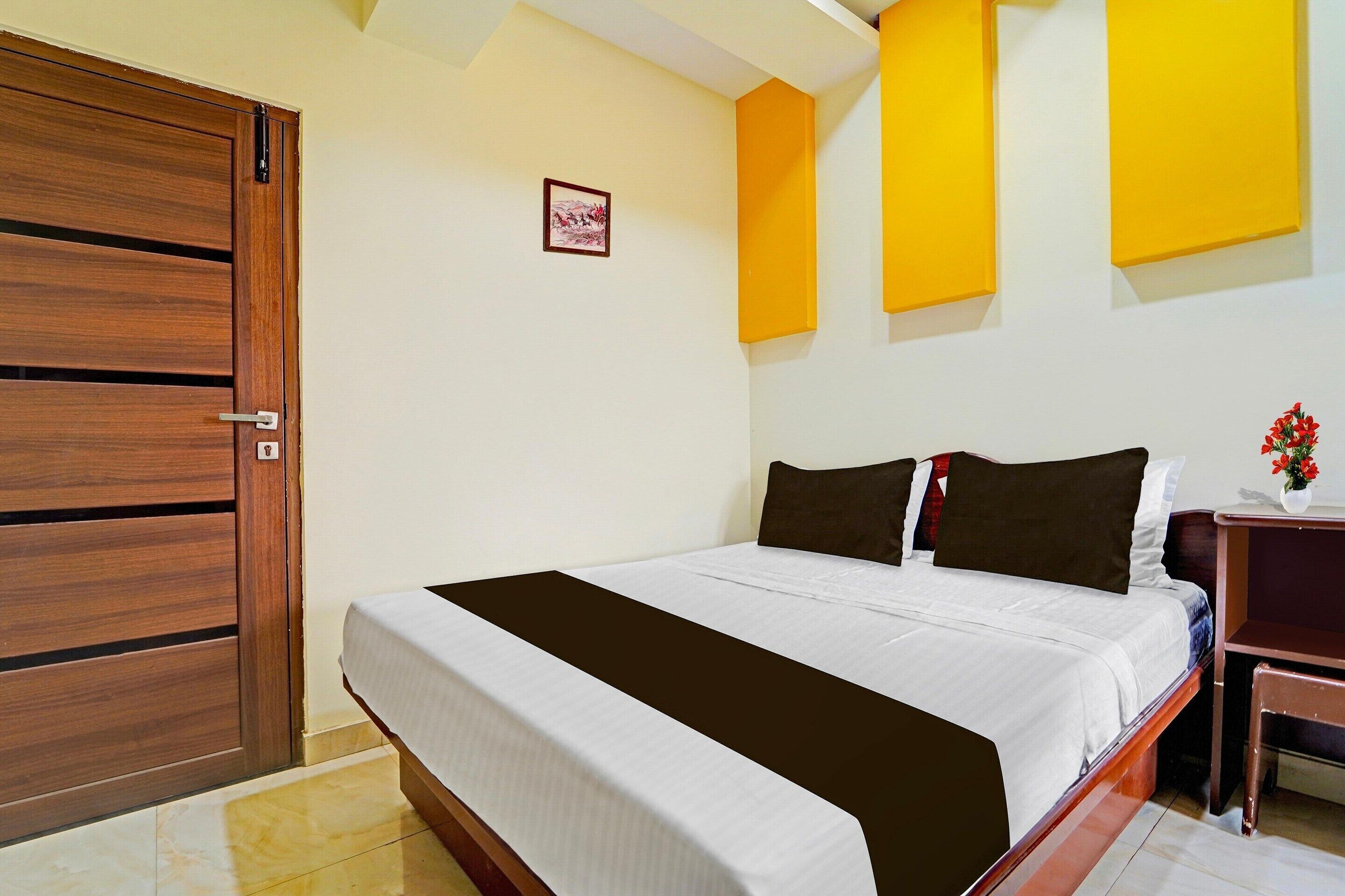Una habitación de hotel con cama, armario de madera y una mesita con un jarrón de flores.
