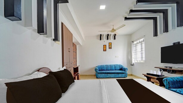 A hotel room with a bed, a blue sofa, a TV, and a ceiling fan. - Deluxe G K Building (Thindukkal)