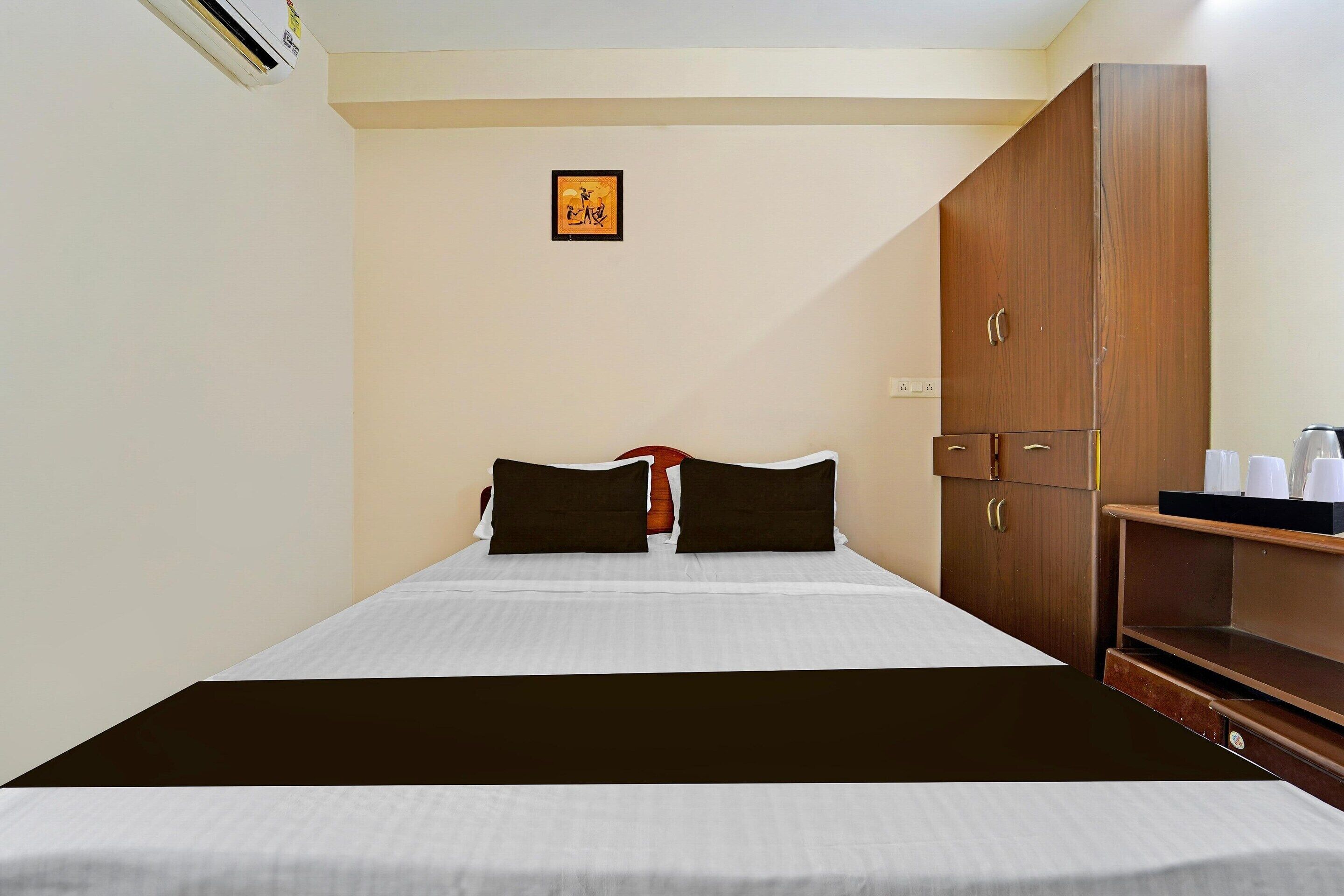 Een hotelkamer met een bed, een kledingkast, een klein tafeltje met kopjes, en een lijst aan de muur.