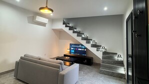 Una sala de estar moderna con un sofá gris, un televisor de pantalla plana y una escalera de diseño único.