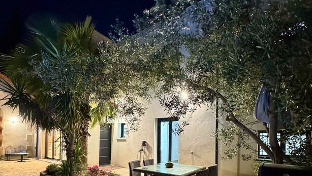 Un patio al aire libre con piso de piedra, una mesa con sillas y un edificio con puerta y ventanas.