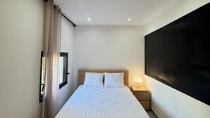 Un dormitorio moderno con cama, mesita de noche y un televisor grande montado en la pared.