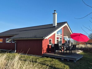 A red house with a chimney, a deck with outdoor furniture, and a large red umbrella. - 4 Star Holiday Home in Grossenbrode (Grossenbrode)