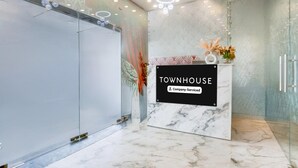 Un área de recepción con mostrador de mármol, pared de vidrio y un letrero que dice 'TOWNHOUSE Company-Serviced'.