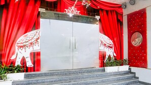 Una escalera conduce a una puerta doble con un panel de vidrio, cortinas rojas y una pared con un emblema circular.