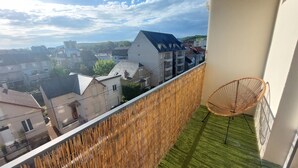 A balcony with a view of a residential area, a wicker chair, and a bamboo fence. - Le Cosy Gaillard, 3 stars. City view and private parking space. (Brive-la-Gaillarde)